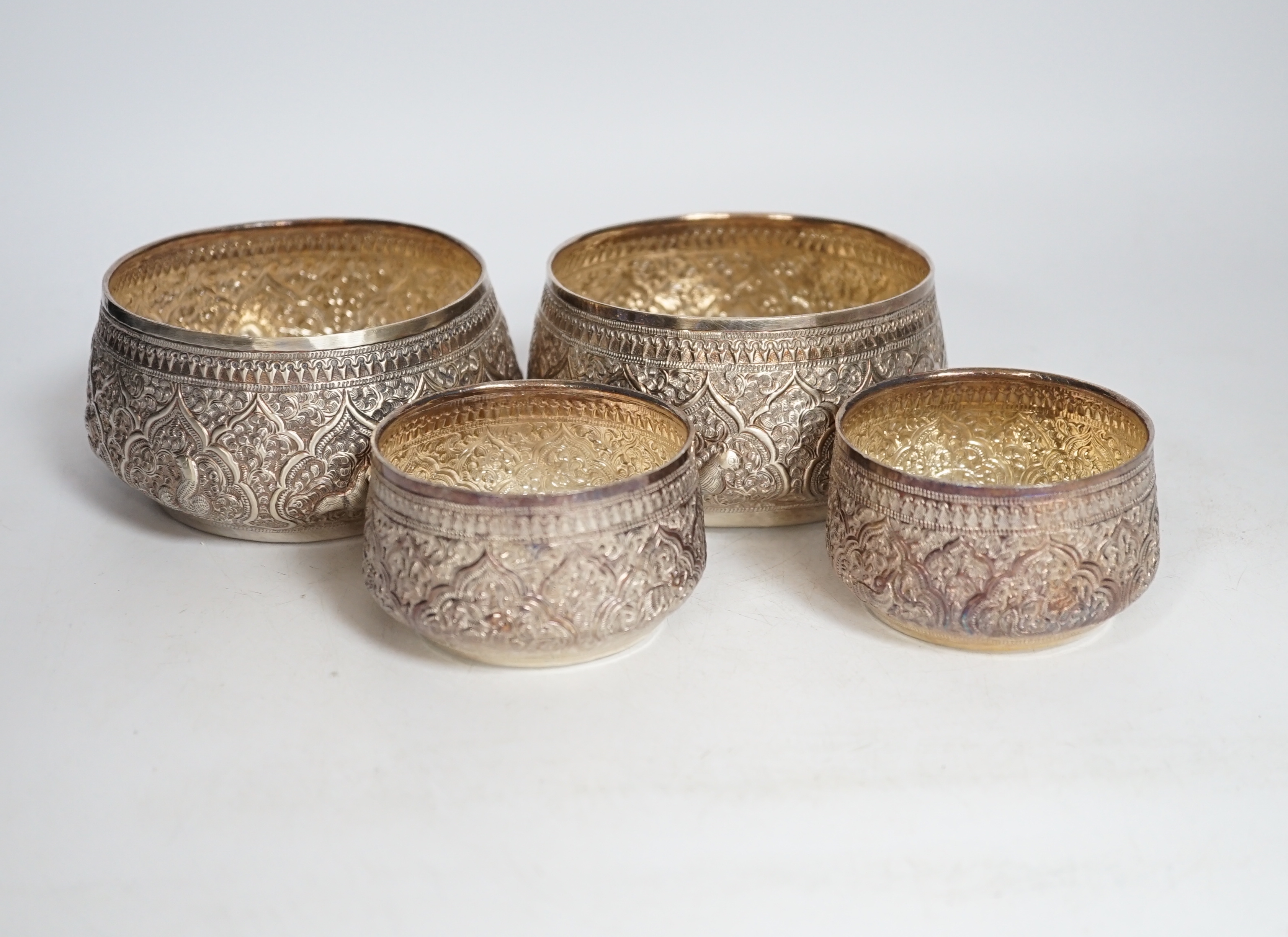 A pair of Thai circular white metal bowls, and a pair of small bowls, all decorated with animals and foliate scrolls, inscribed on bases, diameter 12cm and 8.5cm